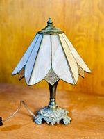 Front view of the stained glass table lamp showing the white and light pink petal-shaped stained glass shade and ornate cast metal base.