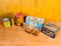Photo of six vintage tins arranged on a wooden surface, showing different sizes and designs including Domestic Shortening and decorative floral tins.