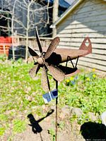 Close-up front angle of the rusted wrought steel biplane wind spinner with propeller blades visible