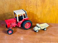 Photo showing both toys: red and beige Ertl International Harvester tractor and yellow Meccano Dinky Euclid dump truck side by side on wooden surface.