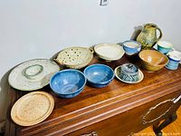All pottery pieces arranged on wooden surface showing variety of shapes and glaze colors including bowls, plates, pitcher, and cups.