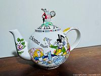 Porcelain teapot with Alice in Wonderland scenes, featuring Alice and the Mad Hatter, side view showing White Rabbit lid and floral spout decoration.