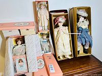 Photo showing vintage porcelain dolls in original boxes, each doll dressed in detailed period-style costumes and wrapped in tissue paper for mint preservation.