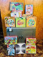 Full view of vintage puzzles stacked on cabinet, many Whitman brand including Flintstones, Smurfs, Bugs Bunny, kitten and more