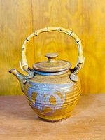 Front view of brown hand-thrown stoneware teapot with natural bamboo handle and decorative glaze pattern.