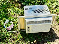 Noma window air conditioner unit shown from top angle with power cord and side panels extended, set on grass.