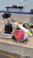 Kitchen set on table including black blender, ceramic cannisters, rolling pin, cookie cutters, and bakeware items