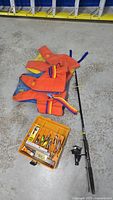 Overview of the fishing rod, two life jackets, and yellow tackle box on concrete floor