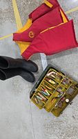 Photo showing large red and yellow life jacket, size 10 black rubber boots, and yellow tackle box opened with visible fishing lures.