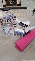 Overview photo of all items showing yoga mat, massager in box, yoga block, butterfly bag, figure skates with guards on concrete floor.