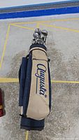 Full view of beige and navy blue Augusta golf bag standing upright with clubs inside.