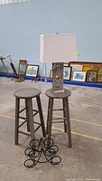 Photo showing two grey wooden bar stools, one with a lamp on top, and a black metal wine rack on the floor.