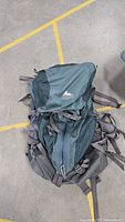 Full view of a grey hiking backpack with multiple straps, buckles and zipper pockets, laid flat on the ground.