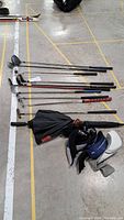 Golf clubs and accessories laid out on floor showing variety of clubs including putters, irons, drivers, club covers, and umbrella.