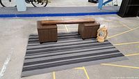 Live edge wooden board placed across two brown padded storage boxes on gray striped rug with wooden lamp next to it in parking lot