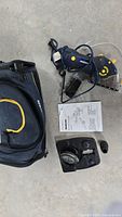 Photo showing Mastercraft blue multi-cutter power saw with yellow button, attached circular saw blade and transparent guard, black and yellow carrying case, additional saw blade component in plastic box, instruction manual on a concrete floor.
