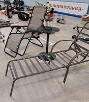 Photo showing 0 gravity recliner, metal chaise lounge, small decorative metal table with lantern/holder on top in indoor setting.