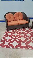 Brown resin wicker loveseat positioned on red and white patterned rug