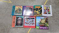 The lot of 7 assorted jigsaw puzzles arranged on the floor, colorful box covers visible.
