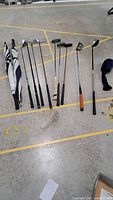Wide view of all golf clubs and two umbrellas laid out on floor showing variety of clubs and accessories