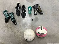 Photo showing 3 pairs of soccer cleats, kids shin pads, soccer ball, volleyball, water bottle, and shoe stand arranged on the floor.