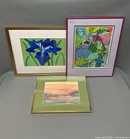 Group shot of three framed watercolor paintings, showing floral, leaf pattern, and landscape subjects