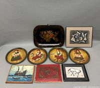 Photo showing all nine pieces of hand painted artwork and decorative items including plates, tray, lithograph, red wood carving, and framed drawing.