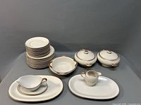 Full view of collection showing stack of plates, two covered serving dishes, creamer jug, small cup and saucer, and platters.