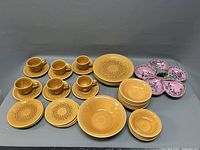 Overview of the ceramic set including six cups and saucers, dinner plates, smaller plates, shallow bowls, and the pink multi-section serving dish.
