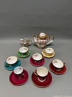 Full tea set with teapot, creamer, six cups, and six saucers in varied colors arranged on a neutral background