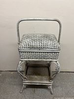 Front view of the wicker sewing basket with handle and hinged lid, showing light wear and distressing.