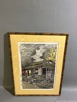 Framed hand-colored Japanese woodblock print depicting a traditional home with smoke from a chimney and two figures at the doorway.