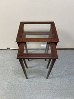 Pair of rectangular wooden framed nesting tables with clear glass tops, stacked showing smaller table fitting under larger.