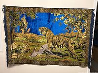 Full view of vintage tapestry depicting tiger, deer, elephant, and humans in natural landscape with blue background and decorative border.