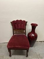 Full view of the wooden chair with red velvet upholstery and the lacquered vase beside it.