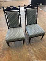 Pair of antique slipper chairs with dark wood frames, turned spindle posts, ornate carved crests, and blue floral upholstery.