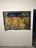 Full view of the tapestry showing three deer in a forest scene with detailed background and ornate border, hanging on a wall.