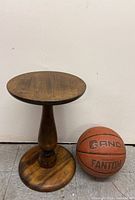 Photo showing full side view of round wooden pedestal next to a basketball for size reference.