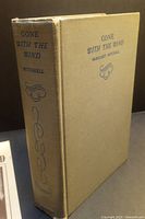 Cloth-bound hardcover novel Gone with the Wind by Margaret Mitchell, beige with blue text and decorative motifs, showing minor wear.
