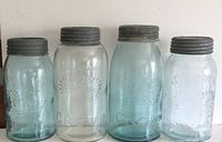 Four antique Crown and North American Glass Co. quart and half-quart sealers with glass lids, showing condition, tint and embossing.