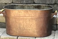 Side view of antique copper boiler showing rectangular shape and wooden handles.