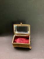 Front angled view of antique French jewelry box with open bevelled glass lid showing red tufted silk lining and gold ormolu embossed base.
