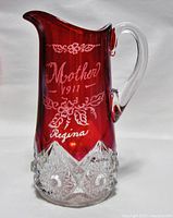 Full view of the tall ruby red flashed glass pitcher with clear handle and pressed glass base, showing overall condition and shape.