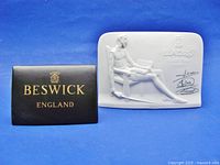 Frontal view of Beswick ceramic retailer sign in matte brown with gold lettering and Lladro bisque porcelain plaque featuring Don Quixote in relief with signatures and logo.