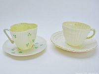 Two Irish Belleek porcelain cups and saucers, limpety yellow and harp shamrock designs, shown side by side.