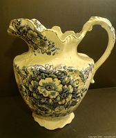 Full view of the large antique porcelain pitcher with blue floral flow blue decoration, scalloped rim and ornate handle.