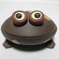 Front view of whimsical dark brown pottery frog with large eyes and cream and yellow spots.