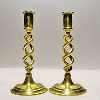 Front view of both brass candle holders, showcasing the twisted open design and polished brass finish.