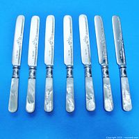 Top view showing all seven cutters with mother-of-pearl handles and engraved blades aligned parallel on blue background.