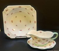 Photo of gravy boat with floral rosebud pattern, green handle and matching underplate, both set on black surface.